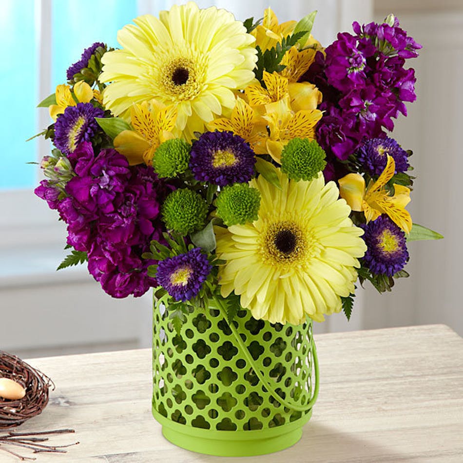 Purple and yellow flowers in a green lantern vase.
